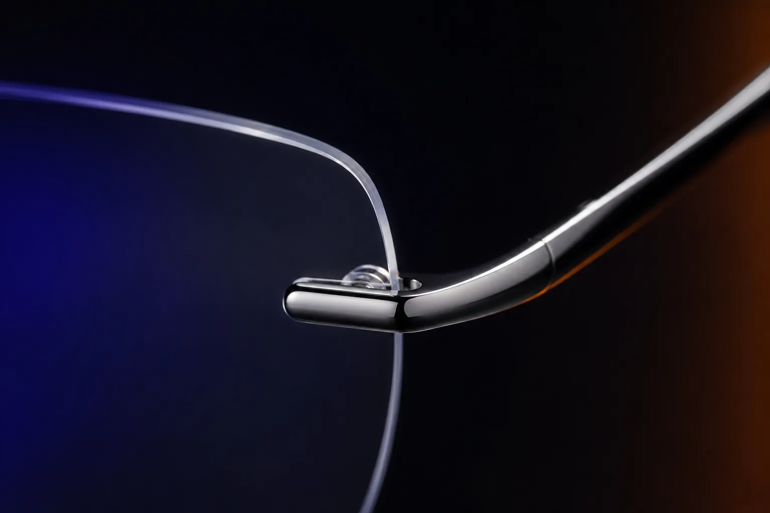 Macro close-up of a rimless lens mount, where a slim polished metal endpiece attaches directly to the clear lens edge with a small fixture and nose-pad arm.