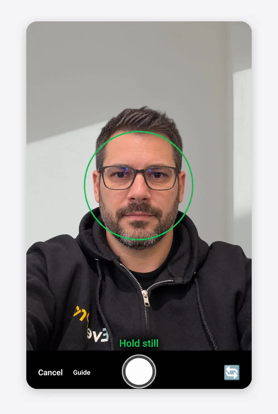 Optogrid app camera view with a green head position ring around the face and the Hold still prompt